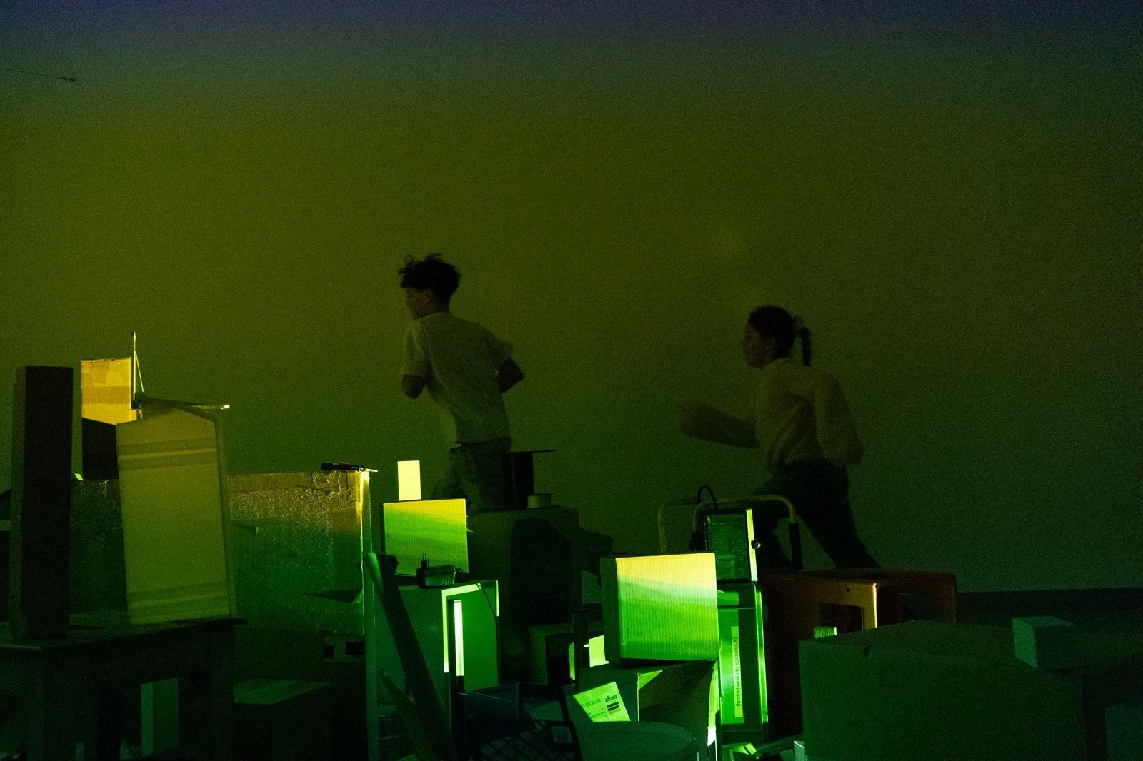 Zwei Performer vor Neonlichtern auf einer dunklen Bühne